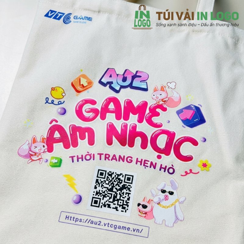 Túi vải canvas trắng in logo VTC Game và thông điệp Au2 Game Âm Nhạc với màu sắc sống động, hình ảnh nhân vật hoạt hình, kèm mã QR và URL, minh họa tiêu chí in ấn chất lượng cho quà tặng doanh nghiệp.