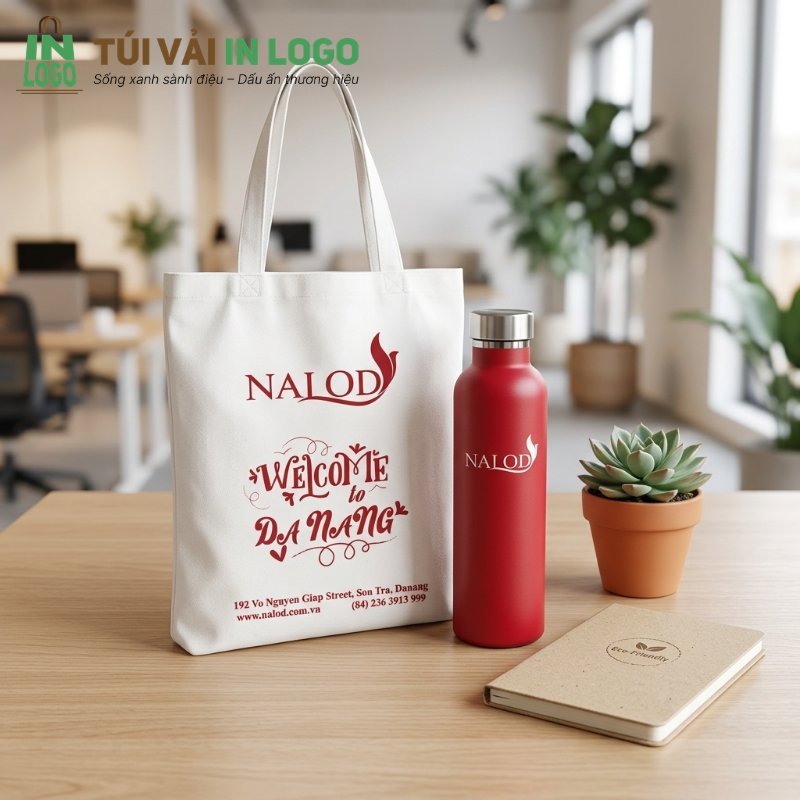 Giftset quà tặng doanh nghiệp sáng tạo bao gồm túi vải canvas in logo NALOD 'Welcome to Da Nang', bình giữ nhiệt đỏ và sổ tay eco-friendly, đặt trên bàn làm việc, thể hiện sự chuyên nghiệp và thân thiện môi trường.