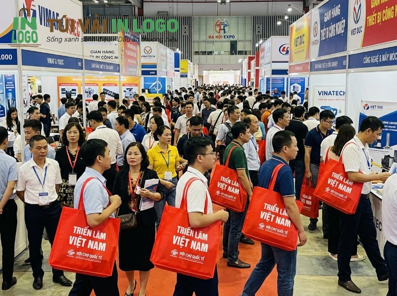 Khách tham quan tại triển lãm đông đúc mang túi vải in logo màu đỏ "Triển lãm Việt Nam" làm quà tặng sự kiện, thể hiện tính ứng dụng và hiệu quả của túi vải in logo trong quảng bá thương hiệu.